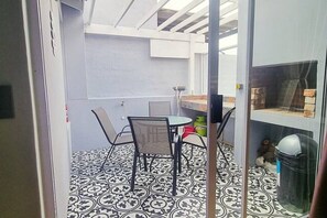 A room with a patterned floor, a table with chairs, a window with a view, and a door.