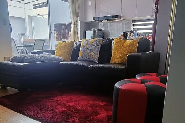 A living room with a sofa, red carpet, and kitchen area in the background.