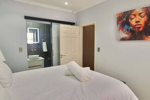 A bedroom with a bed, a bathroom with a sink and mirror, and a door.
