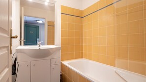 Ein Badezimmer mit weißem Waschbecken, einer Badewanne und gelben Fliesen.