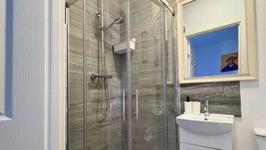 Un baño moderno con cabina de ducha de vidrio, un lavamanos blanco y un espejo encima.