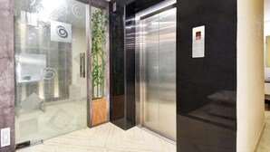 A modern elevator with a digital display, a glass door with a reflection, and a potted plant beside it.