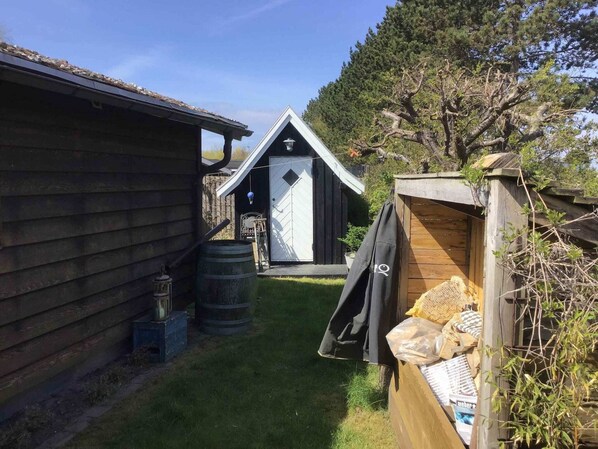 A wooden cabin with a small attached shed, a barrel, and a garden area. - 4 Star Holiday Home in Karrebaeksminde (Karrebæksminde)