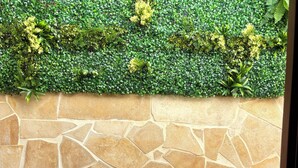 Un muro de piedra con un seto verde en la parte superior y una mesa de madera al frente.