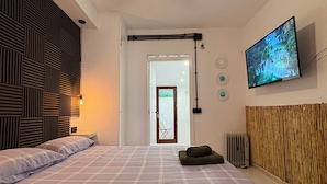 Un dormitorio con cama, ventilador de techo, televisor y una puerta que da a otra habitación.