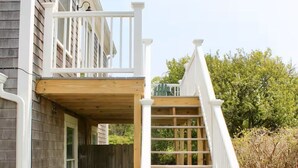Een huis met twee verdiepingen, een houten terras en een witte trap die naar de bovenverdieping leidt.