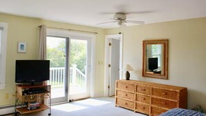 Een kamer met een televisie op een standaard, een rieten dressoir, een plafondventilator en een schuifdeur naar een balkon.
