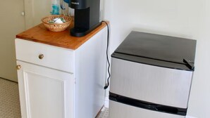 Een kitchenette met een koffiezetapparaat, een kleine koelkast en een mandje op een houten aanrecht.