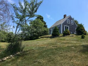 Une maison avec un toit en pente, entourée d’une pelouse bien entretenue et de plusieurs arbres.