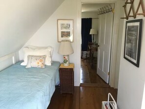 Une chambre à coucher avec un lit, une table de chevet avec une lampe, un tableau encadré au mur et une porte donnant sur une autre pièce.