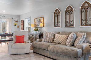 A living room with a striped armchair, a beige sofa with patterned cushions, a dining area with a table and chairs, and decorative wall art. - Trolly Inn Hot Tub, Walkable (Branson)
