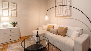 Ett modernt vardagsrum med en soffa, ett soffbord i glas, ett sidobord med en lampa och inramade tavlor på väggen.