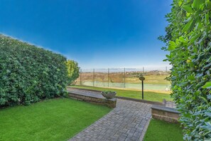 Ein gepflasterter Weg führt zu einer grünen Fläche mit Blick auf einen Golfplatz.