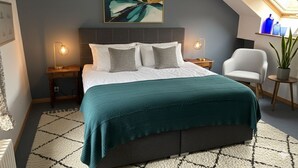 A bedroom with a bed, two bedside tables, a chair, a potted plant, and a skylight. - Les Vieux toits (Hauterive)