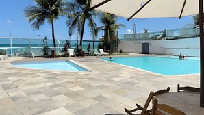 Una piscina con sillones de descanso, palmeras y vistas al océano.