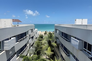 Um hotel moderno com vista para a praia, com varandas, piscina e plantas tropicais.