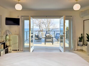 Une chambre dotée d’un grand lit, d’une télévision, d’un radiateur et offrant une vue sur un balcon avec des sièges d’extérieur.