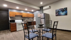 A modern kitchen with wooden cabinets, a stainless steel refrigerator, and a glass dining table with four chairs. - Oceanview Modern Guest House With Pool (Sardinal)