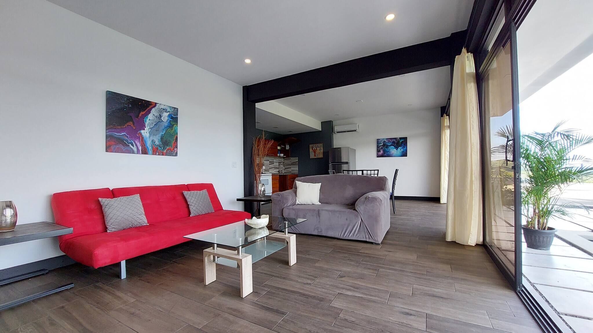 A modern living room with a red sofa, a grey sofa, a glass coffee table, and artwork on the walls.