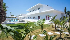 A modern white building with a pool, palm trees, and a clear blue sky. - 14 Ground Floor (Faliraki)