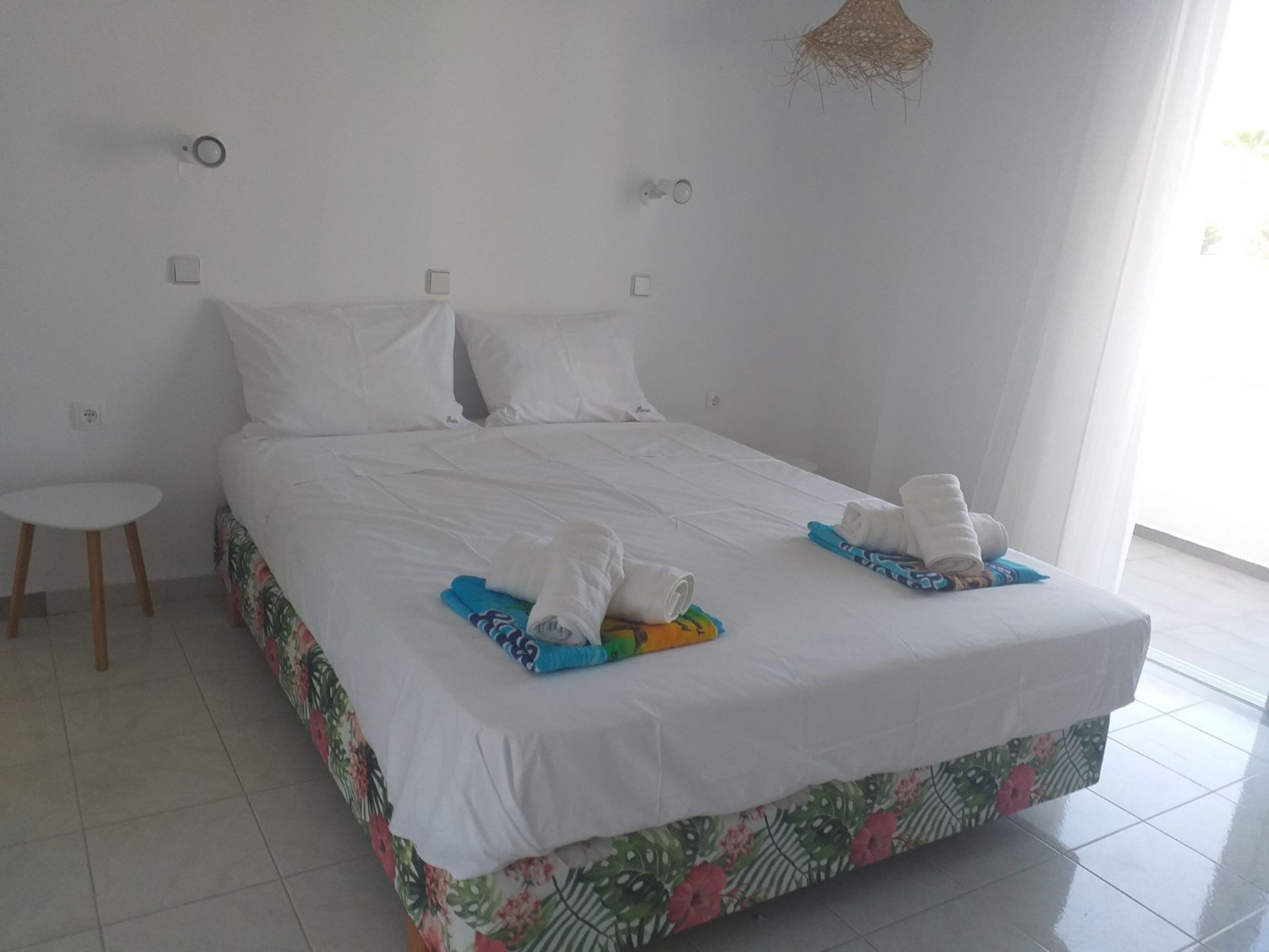 Une chambre d’hôtel avec un grand lit, une petite table et un luminaire suspendu.