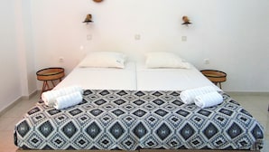 Een tweepersoonsbed met een gebedruid sprei, twee witte kussens, twee nachtkastjes met gevlochten manden en twee wandspiegels.