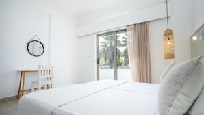 A bedroom with a bed, a chair, a desk, a window with curtains, and a hanging light fixture. - 10 Ground Floor (Faliraki)