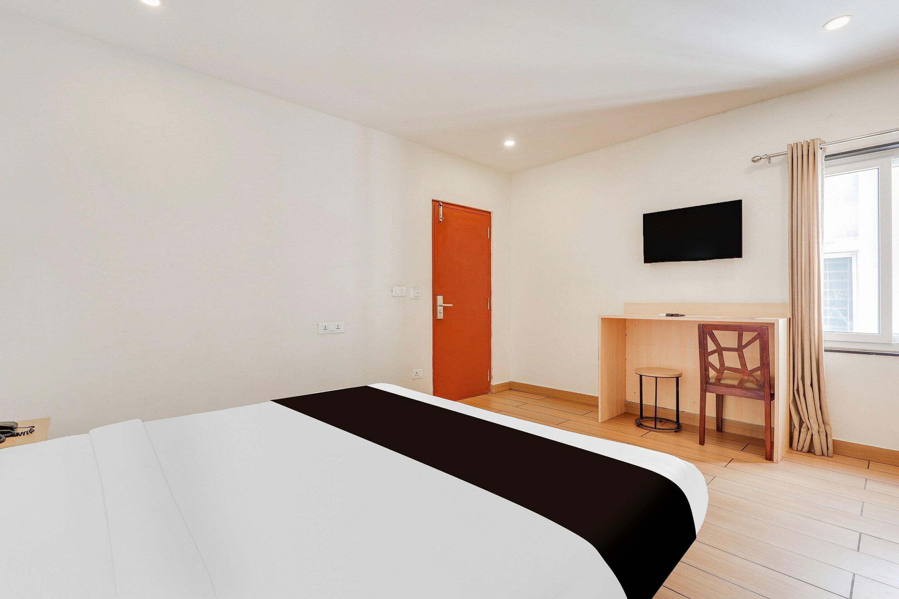 Ein Hotelzimmer mit Bett, Schreibtisch, Stuhl, Fernseher und einem Fenster mit Vorhängen.