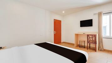 Ein Hotelzimmer mit Bett, Schreibtisch, Stuhl, Fernseher und einem Fenster mit Vorhängen.