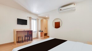 A hotel room with a bed, a desk with a chair, a television, an air conditioning unit, and a door. - Deluxe With Twin Bed The Pallagio (Visakhapatnam)