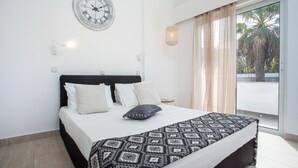 A bedroom with a bed, a wall clock, a window with curtains, and a view of palm trees. - 11 Ground Floor (Faliraki)