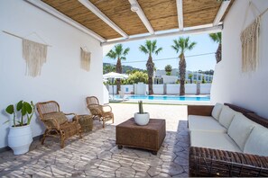 Eine sonnendurchflutete Terrasse mit Korbmöbeln, einem weißen Sofa und einem Blumentopf.