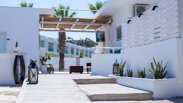 A modern outdoor area with a concrete pathway, a wooden pergola, and a seating area with a bench and chairs. - 107 First Floor (Faliraki)