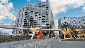 Un bâtiment moderne doté d’une façade en verre, d’une promenade piétonne et d’une structure rouge distinctive.
