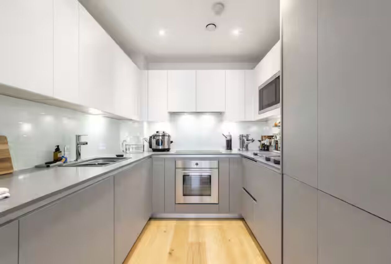 Una cucina moderna con mobili grigi, elettrodomestici in acciaio inossidabile e pavimento in legno.