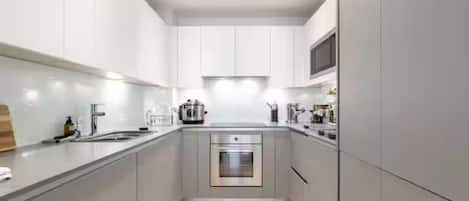 Une cuisine moderne avec des meubles gris, des appareils en acier inoxydable et un plancher en bois.