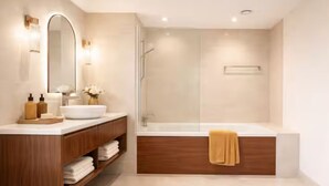 Ein modernes Badezimmer mit einem Holzkosmetikschrank, einem großen Spiegel, einem weißen Waschbecken und einer Duschkabine.