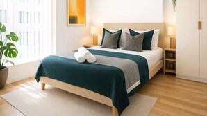 Ein ordentlich eingerichtetes Schlafzimmer mit Bett, Nachttischlampen, einem Topf mit Pflanze und einem Bild an der Wand.