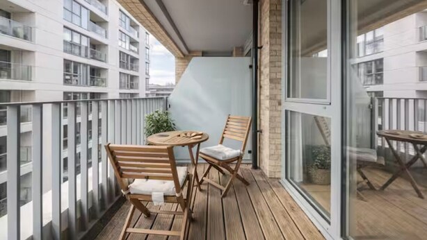 Ein Balkon mit Tisch und Stühlen, einer Topfpflanze und Blick auf angrenzende Gebäude.