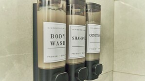 Tre flaconi di bagnoschiuma, shampoo e balsamo su un dispenser a parete.