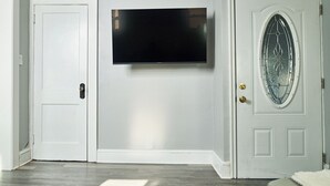 Un corridoio con una porta bianca, una porta con un pannello di vetro e un televisore a schermo piatto montato al muro.
