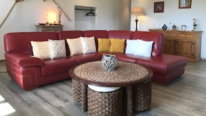 A red leather sofa with patterned cushions, a woven coffee table, a wooden cabinet, and wall-mounted artwork.