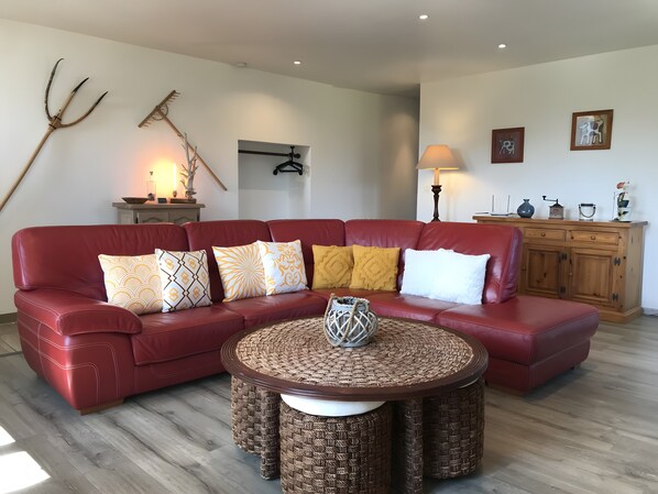 A red leather sofa with patterned cushions, a woven coffee table, a wooden cabinet, and wall-mounted artwork.