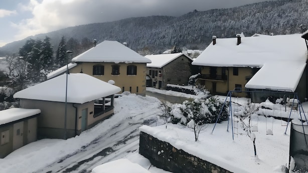A snow-covered village with traditional buildings, a stone wall, and a clear view of the surrounding mountains.