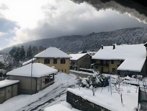 A snow-covered village with traditional buildings, a stone wall, and a clear view of the surrounding mountains.