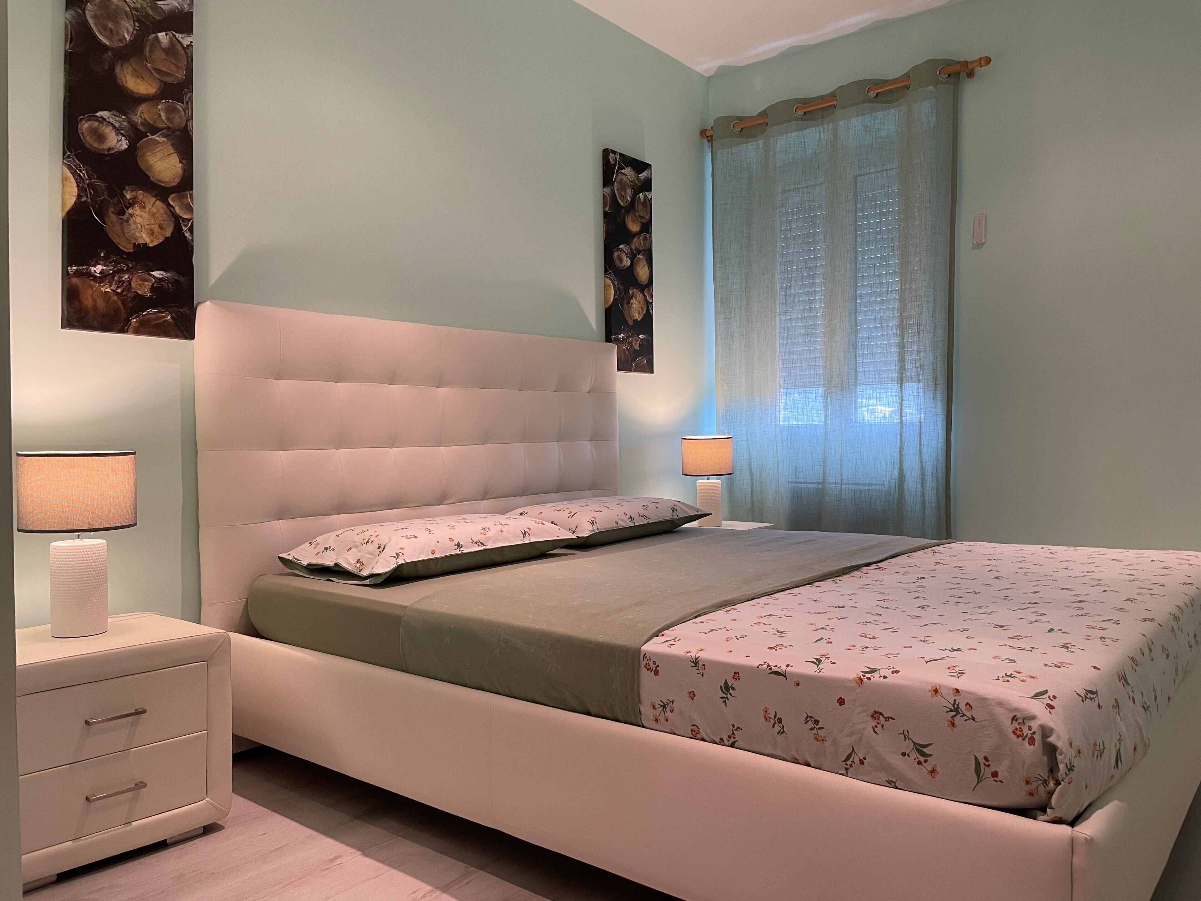 A bedroom with a bed, bedside lamps, a nightstand, and a wall with a floral pattern.