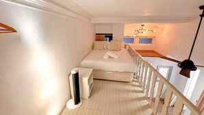 Ein Schlafzimmer mit Bett, Heizung, Deckenventilator und Blick auf eine Küche.