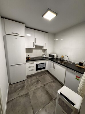 Eine moderne Küche mit weißen Schränken, einem Kühlschrank, einer Mikrowelle, einem Toaster und einem Geschirrspüler.