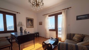 A living room with a piano, a sofa, a coffee table, and a view of the sea. - Dual bay views by ΜΡS (Μαρίστρα)
