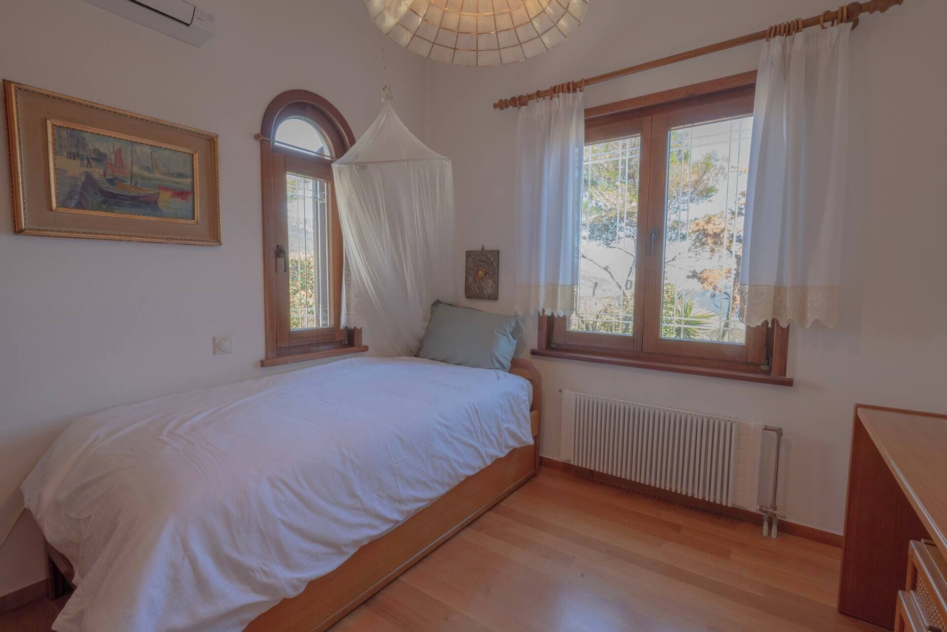 Ein Schlafzimmer mit einem Bett, zwei Fenstern, einem Heizkörper und einem Bild an der Wand.